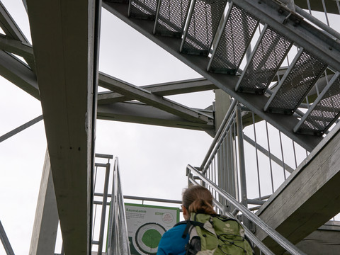 Aufstieg Weifbergturm Person steigt Außentreppe mit Metallgeländer hoch, bewölkt.
