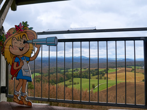 Zwischenstation Weifbergturmaufstieg Maskottchen von Sebnitz mit Fernrohr blickt von Balkon auf Landschaft.