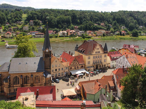 Blick auf eine kleine Stadt am Flussufer mit Kirche, bunten Häusern und grünen Hügeln.View of a small riverside town with a church, colorful houses and green hills.Pohled na městečko na břehu řeky s kostelem, barevnými domy a zelenými kopci.Widok na małe nadrzeczne miasteczko z kościołem, kolorowymi domami i zielonymi wzgórzami.Uitzicht op een klein stadje aan de rivier met een kerk, kleurrijke huizen en groene heuvels.Vista di una piccola città sul fiume con una chiesa, case colorate e colline verdi.