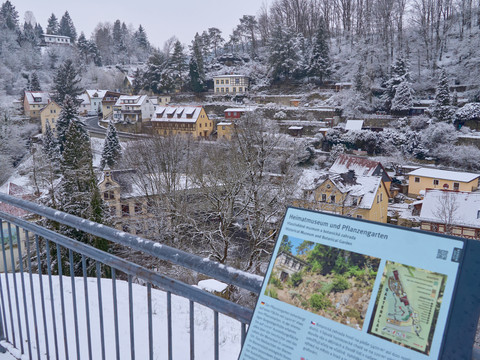 Winterliche Aussicht auf ein verschneites Dorf mit Informationskarte im Vordergrund.Winter view of a snow-covered village with information map in the foreground.Zimní pohled na zasněženou vesnici s informační mapou v popředí.Zimowy widok ośnieżonej wioski z mapą informacyjną na pierwszym planie.Winteraanzicht van een besneeuwd dorp met informatiekaart op de voorgrond.Veduta invernale di un villaggio innevato con mappa informativa in primo piano.