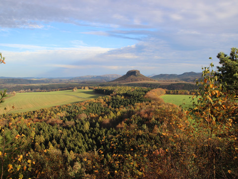 Herbstliche Landschaft mit bewaldeten Hügeln und einem markanten Berg im Hintergrund.