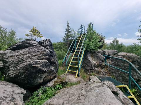 Gelbe Metallleiter zwischen großen Felsen unter bewölktem Himmel.