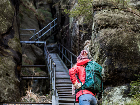 Person in roter Jacke steigt steile Treppe in felsiger Schlucht hoch.