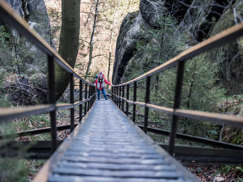 Person wandert eiseren Treppe bergan in einem bewaldeten Schluchtgebiet.