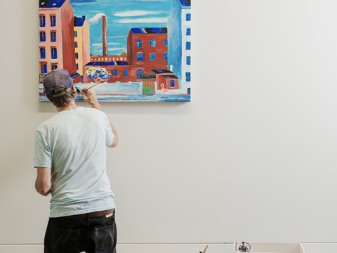 KSC_GUN_Best of II_Turek_Wunderwald_2025_FotoMarkFrost.jpg Ein Künstler malt kniend ein farbenfrohes Stadtbild an einer weißen Wand.An artist kneels and paints a colorful cityscape on a white wall.Umělec klečí a maluje na bílou zeď barevnou krajinu města.Artysta klęczy i maluje kolorowy pejzaż miejski na białej ścianie.Een kunstenaar knielt en schildert een kleurrijk stadsgezicht op een witte muur.Un artista si inginocchia e dipinge un paesaggio urbano colorato su un muro bianco.