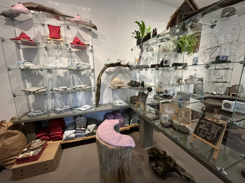 Devona Shop Ein kleiner, geschmackvoll eingerichteter Laden mit Glasregalen, die handgefertigte Produkte präsentieren. Pflanzen schmücken die Ecken.