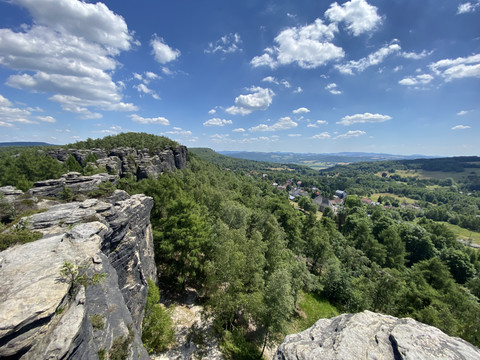 Aussicht von felsigem Berg auf bewaldete Landschaft und blauen Himmel.