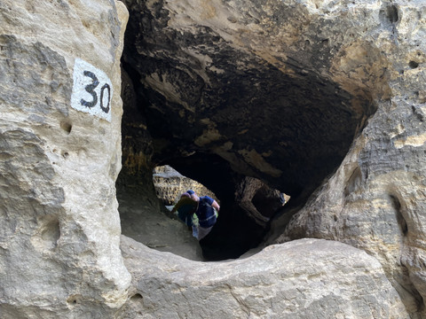 Felsenhöhle mit der Nummer 30, Person in blauer Jacke erkundet den Eingang.