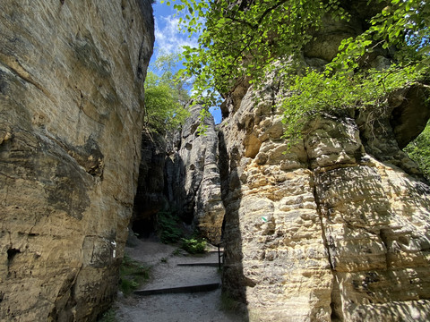 Schmaler Wanderweg zwischen hohen Felswänden unter blauem Himmel.