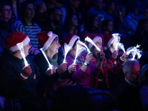 Oberberg singt Besucher einer Veranstaltung tragen Nikolausmützen und leuchtende Faseroptikstäbe in den Händen.
