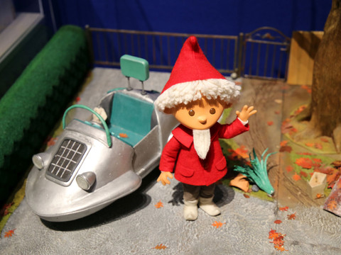 1 - Sandmännchen in Leipzig - Foto Andreas Schmidt.jpg Das Sandmännchen in rotem Mantel und Zipfelmütze winkt neben einem kleinen silbernen Auto.The Sandman in his red coat and pointed cap waves next to a small silver car.Písečný muž v červeném kabátě a špičaté čepici mává vedle malého stříbrného auta.Sandman w czerwonym płaszczu i spiczastej czapce macha obok małego srebrnego samochodu.De Zandman in een rode jas en puntmuts zwaait naast een kleine zilveren auto.L'Uomo Sabbia in cappotto rosso e berretto a punta saluta accanto a una piccola auto argentata.
