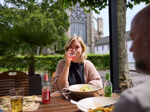 Altenberger Hof Zwei Personen essen draußen an einem Holztisch vor einer großen Kirche im Grünen.
