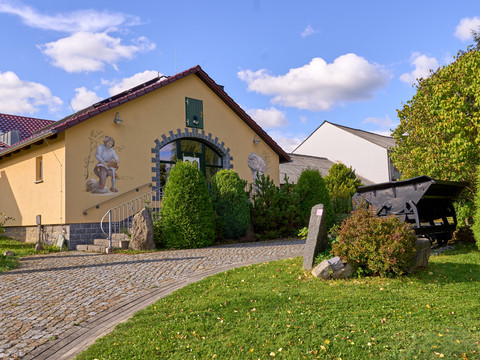 Gold-und-Mineralien-Erlebnisstätte Hohwald bei Neustadt Gelbes Haus mit Torbogen, Bilder an der Wand und gepflastertem Weg.