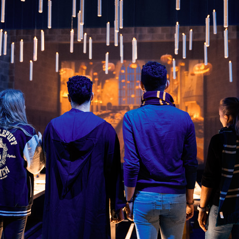Harry Potter - The Exhibition 4 Personen stehen mit dem Rücken zum Fotografen in einer Harry Potter Ausstellung mit fliegenden Kerzen.4 people stand with their backs to the photographer in a Harry Potter exhibition with flying candles.
