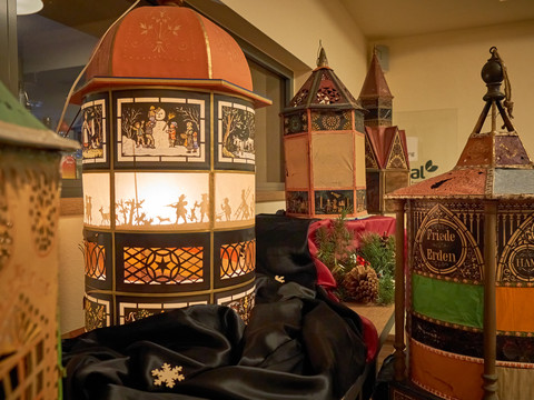 Tannert- Pyramiden Verschiedene beleuchtete Laternen in einem Raum, darunter eine große mit Scherenschnittmotiven.