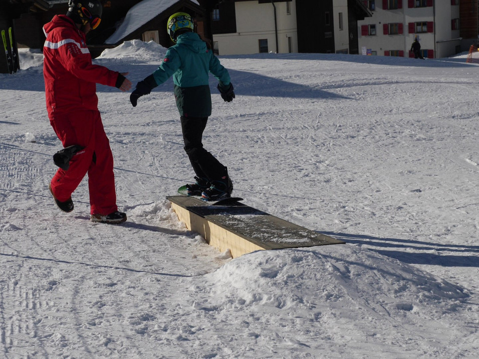 Erste Balanceversuche auf dem Snowboard Kind übt Balance im Snowboard Schnupperkurs Fiescheralp mit Unterstützung eines SkilehrersChild practicing balance on the Fiescheralp snowboard taster course with the support of a ski instructorUn enfant s'exerce à l'équilibre lors d'un cours d'initiation au snowboard à Fiescheralp avec le soutien d'un moniteur de ski