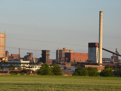 Huettenwerk_Salzgitter_HD_16zu9.JPG Blick auf das Hüttenwerk Salzgitter mit Industrieanlagen, Türmen und Leitungen hinter grünen Feldern.