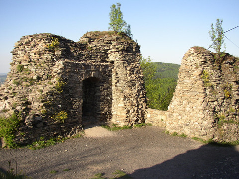Ruinen alter Steinmauern mit Bäumen auf der Spitze, vor bewaldeten Hügeln.