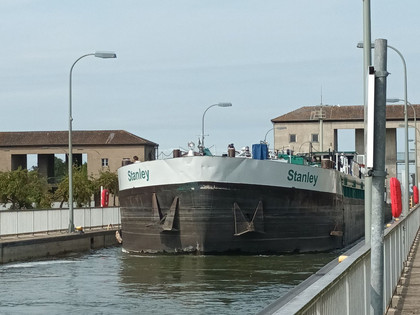 Schleuse Üfingen (87)_HD_16zu9.jpg Ein Frachtschiff in der Schleuse Üfingen, umgeben von Wasser, Schleusenwänden und Betriebsgebäuden.