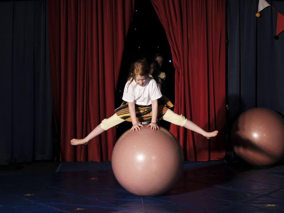 Balancing act on the ball Ein Mädchen zeigt im Mitmachzirkus Aletsch Arena einen mutigen Spagat auf einer grossen rosa Balancierkugel.A girl performs a courageous balancing act on a large pink balancing ball in the Aletsch Arena hands-on circus.Au cirque participatif Aletsch Arena, une jeune fille fait courageusement le grand écart sur une grosse boule d'équilibre rose.