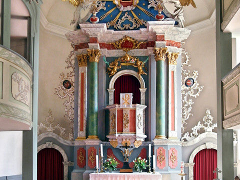 Bunter, kunstvoller Altar mit Säulen, Verzierungen und einem roten Teppich im Kircheninneren.