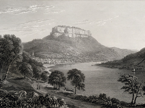 Blick auf einen Fluss mit bewaldeten Ufern und einem markanten, hohen Felsen im Hintergrund.