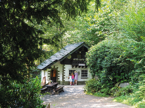 Osterzeit im Märchenwald Kleines Fachwerkhaus im grünen Wald. Drei Kinder stehen vor dem Eingang, ein Holztisch daneben.