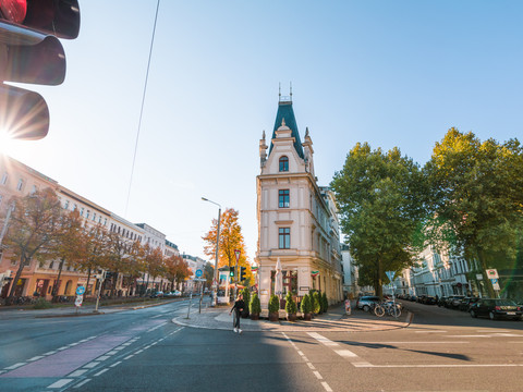 Die Sonne erhebt sich an einem Herbstmorgen mit bunten Bäumen über den Dächern der Häuser auf der noch ruhigen Karl-Liebknecht-Straße in Leipzig