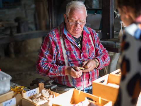 Holzwerkstatt im Freilichtmuseum Ein Mann in rot-blau kariertem Hemd fertigt am Marktstand handwerkliche Holzobjekte.