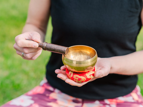 Klangschale - Klangmeditation Eine Person hält eine Klangschale in der Hand und schlägt sie mit einem Holzschlägel an.
