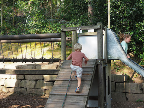 Spielplatz im Märchenwald Altenberg Zwei Kinder spielen an einem hölzernen Klettergerüst mit Rutsche in bewaldeter Umgebung.