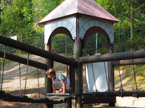 Spielplatz im Märchenwald Altenberg Kind auf hölzerner Hängebrücke unter Spielturm in bewaldeter Umgebung.