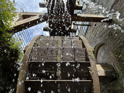 Mühlrad der Papiermühle Großes hölzernes Mühlrad mit herabprasselndem Wasser im Außenbereich einer historischen Mühle