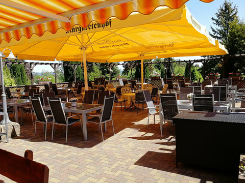 Margaretenhof Sonnenterasse Gedeckte Tische und Stühle unter einem gelben Sonnenschirm in einem Außenbereich eines Restaurants.