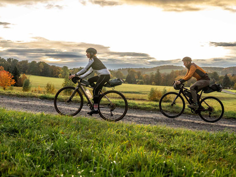 Auf dem RockHead bei Rosenthal-Bielatal Zwei Gravelbiker fahren einen Schotterweg bergauf, im Hintergrund sind Wiesen und Wald zu sehen.