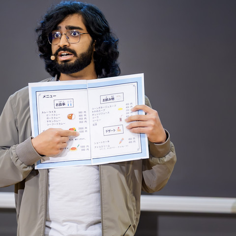 Moksh Bhateja beim FameLab Dresden 2026 Mann hält japanische Speisekarte hoch