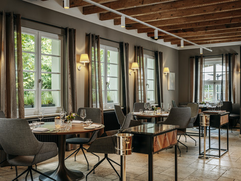 Gourmetrestaurant „Schote“ Eleganter Gastraum mit gedeckten Tischen, großen Fenstern, warmem Licht und Holzbalkendecke