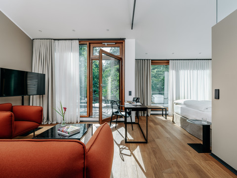 Diepeschrather Mühle Juniorsuite Helle Juniorsuite mit roten Sesseln, großem Bett, Holzboden und bodentiefen Fenstern.