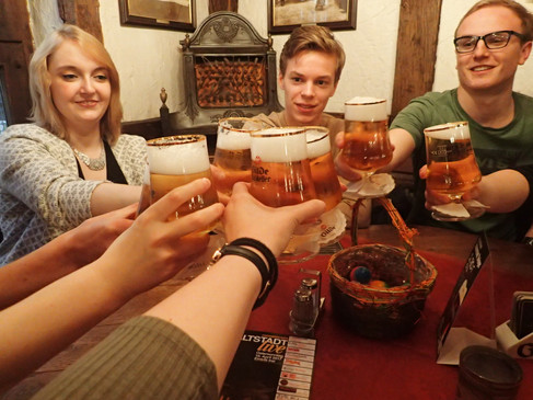 Eine Gruppe junger Leute prostet sich fröhlich mit Gläsern in einer rustikalen Kneipenatmosphäre zu.