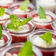 Dessert Mehrere kleine Gläser mit einem roten Dessert und dekorativen Minzblättern auf Sahnetopping.