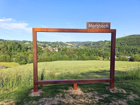 Fotorahmen Heiderberg Metallrahmen mit Morsbach-Schrift vor grünen Hügeln und weitläufiger Landschaft.