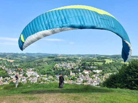 Gleitschirmflieger Hohe Hardt Gleitschirm startet über einer grünen Anhöhe mit weitem Blick auf die umliegende Ortschaft