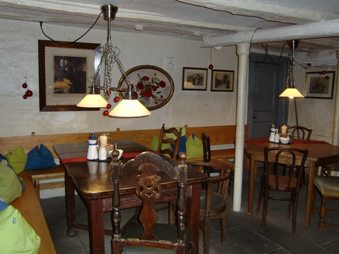 Die gute Stube Gemütliches Cafe mit rustikalen Holzmöbeln, Kissen und Wanddekorationen in warmem Licht.