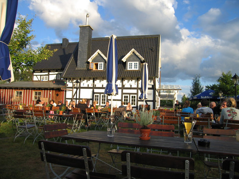 Hielscher Hof Ein idyllischer Biergarten vor einem Fachwerkhaus, Sonnenbeschienene Gäste sitzen an Holzbänken.