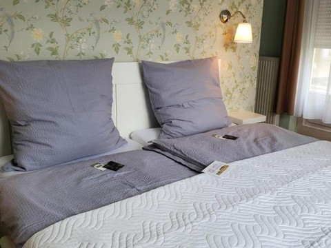 Privatzimmer2_Privatpension Waldbröl Doppelbett mit grauer Bettwäsche, floraler Tapete und Fenster im Privatzimmer