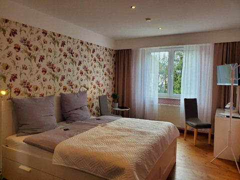 Gästezimmer_Privatpension Waldbröl Gästezimmer mit Doppelbett, Blumentapete, Fenster, Schreibtisch und TV in Waldbröl