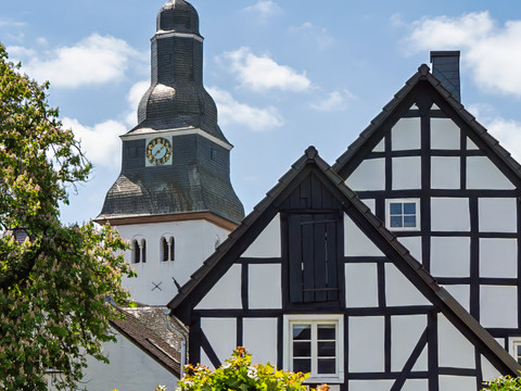 1000-jährige Dorfkiche Kirchturm und Fachwerkhaus im Ortskern von Nümbrecht unter blauem Himmel