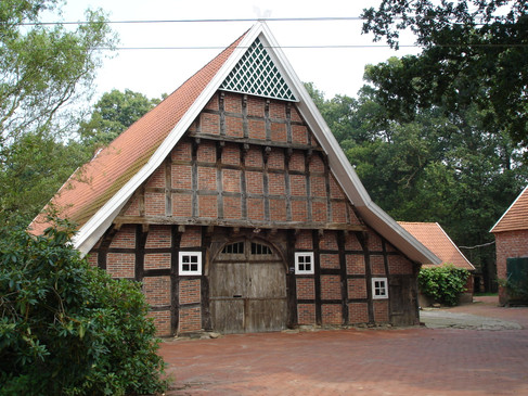 Fietsen op de Giebeltour in het Artland Historisches Fachwerkgebäude mit großem Holztor und Ziegeldach in grüner Umgebung.