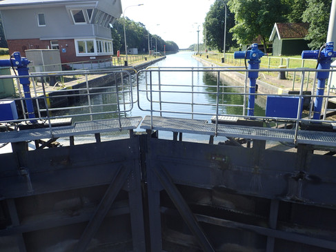 Schleusenanlage mit geöffneten Toren und Blick auf den ruhigen, von Bäumen gesäumten Kanal.
