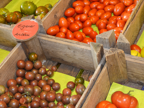 Verschiedene Tomatensorten in Holzkisten auf einem Markt mit Schild "Eigener Anbau".